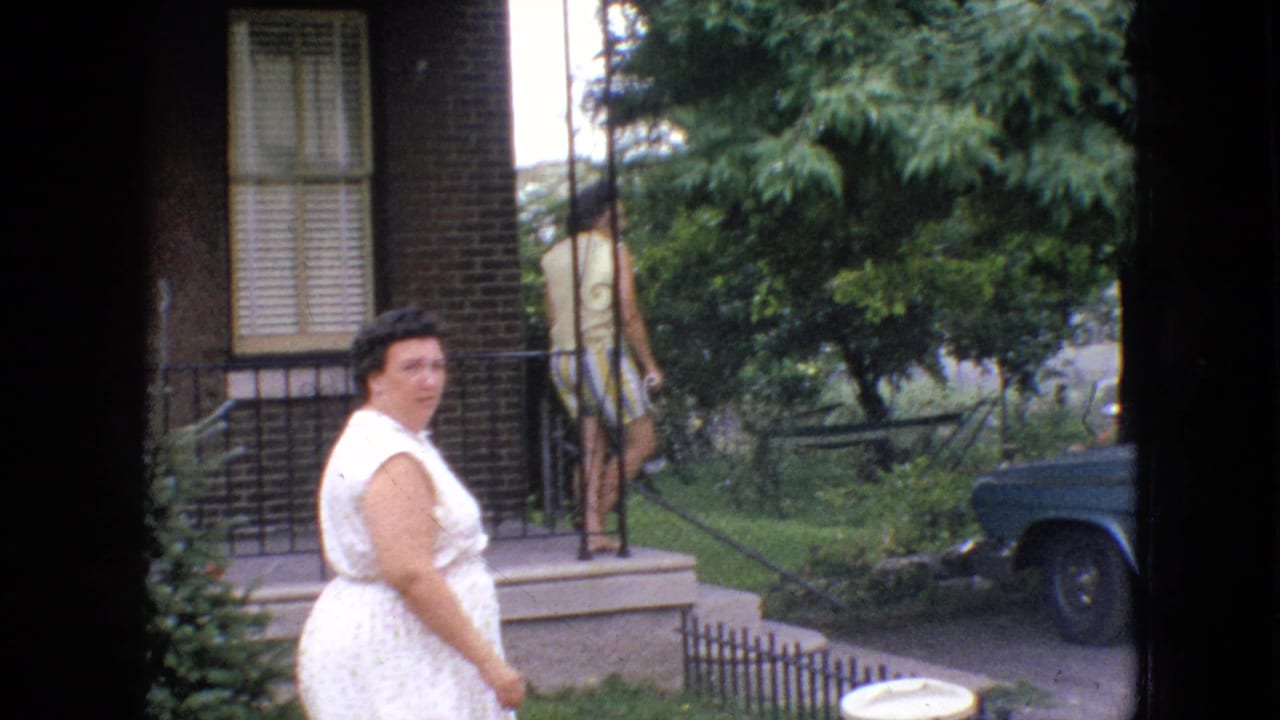 Woman in a white dress standing near a brick porch with trees and a parked car nearby.