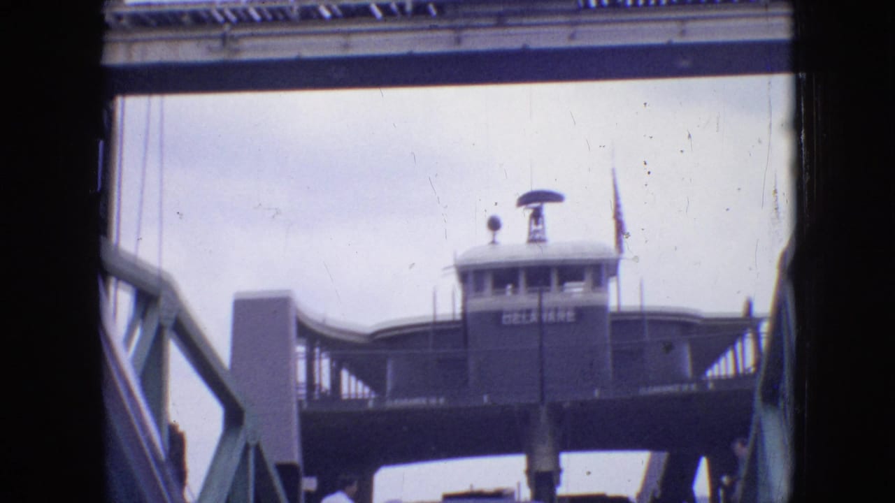 1964 Philadelphia home-movie frame showing a ferry or landing structure viewed from below or from a vessel, with dark edge framing and soft 8mm exposure.