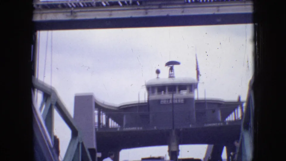 1964 Philadelphia home-movie frame showing a ferry or landing structure viewed from below or from a vessel, with dark edge framing and soft 8mm exposure.