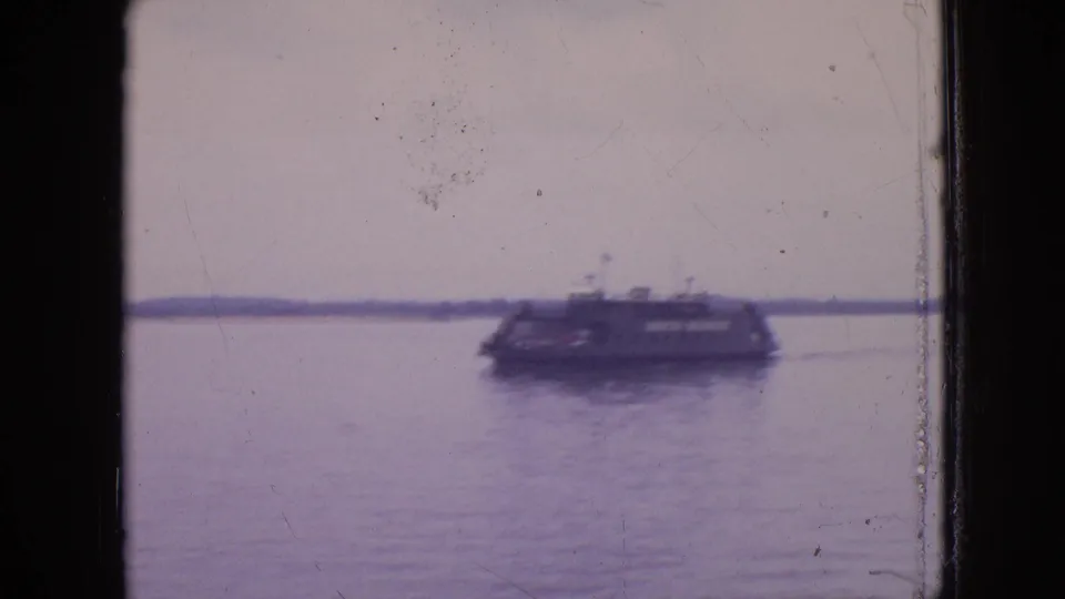A soft-focused ferry-style sightseeing boat moves across still water in 1964 Philadelphia footage, framed by dark film edges and surface scratches.