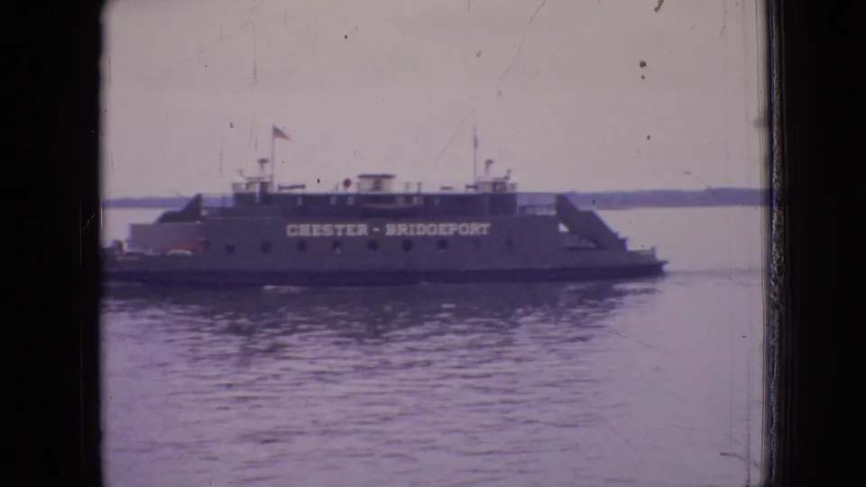 A closer 1964 home-movie view shows the Chester-Bridgeport name clearly painted along the ferry side, with water in the foreground and a low shoreline beyond.