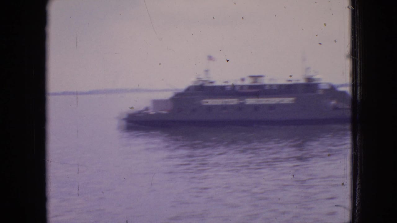 Blurred ferry moving across water with shoreline visible in the distance.
