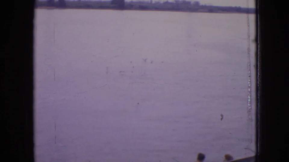 Final 1964 Philadelphia-area frame with the ferry no longer visible, leaving calm water, a distant shoreline, window framing, and aged 8mm surface marks.