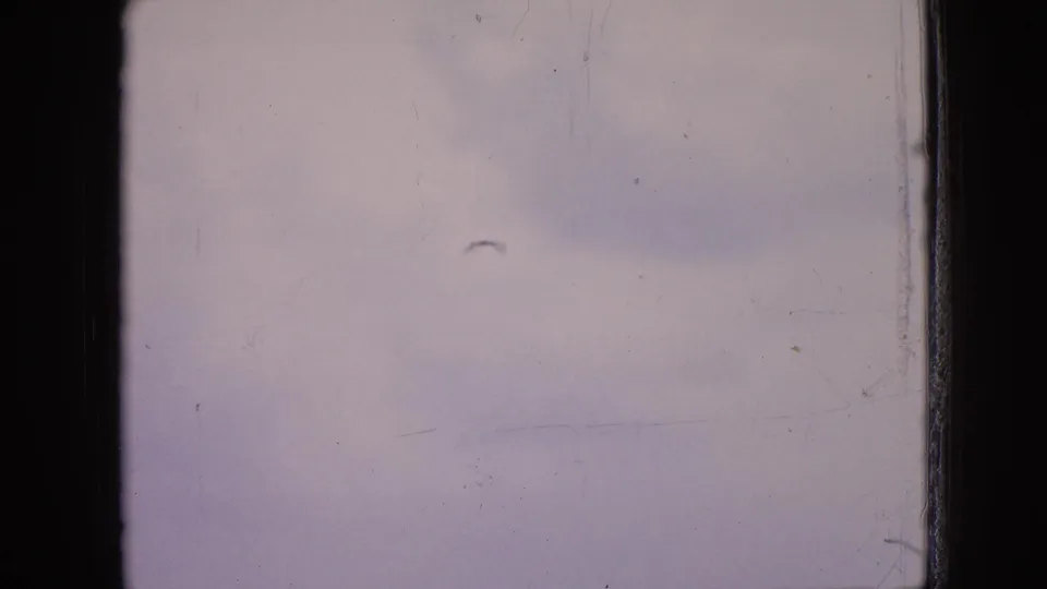 1964 Philadelphia home-movie frame showing a hazy view through dark ferry window framing with faint water and shoreline detail.