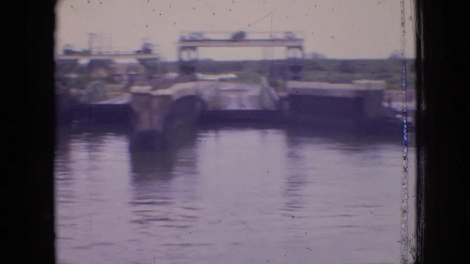 Soft, purple-tinted 8mm view of a Philadelphia canal lock area, with water in the foreground and a raised metal bridge or gate frame spanning the passage.