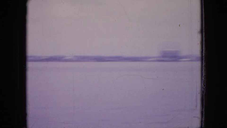 Purple-tinted 1964 8mm view of a distant shoreline across water in the Philadelphia-area clip, framed by dark scan edges.