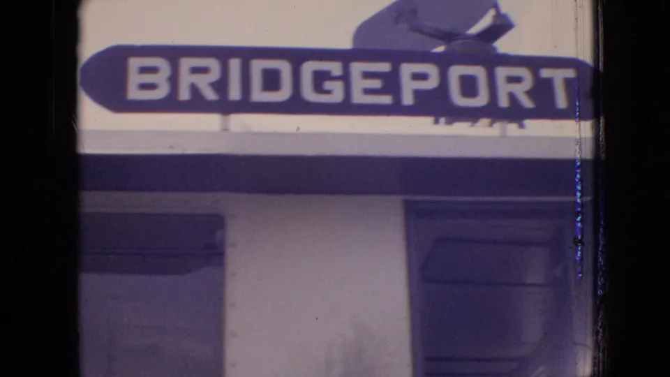 1964 8mm frame showing a bold Bridgeport sign above a building facade, with cropped architectural details and visible film wear.