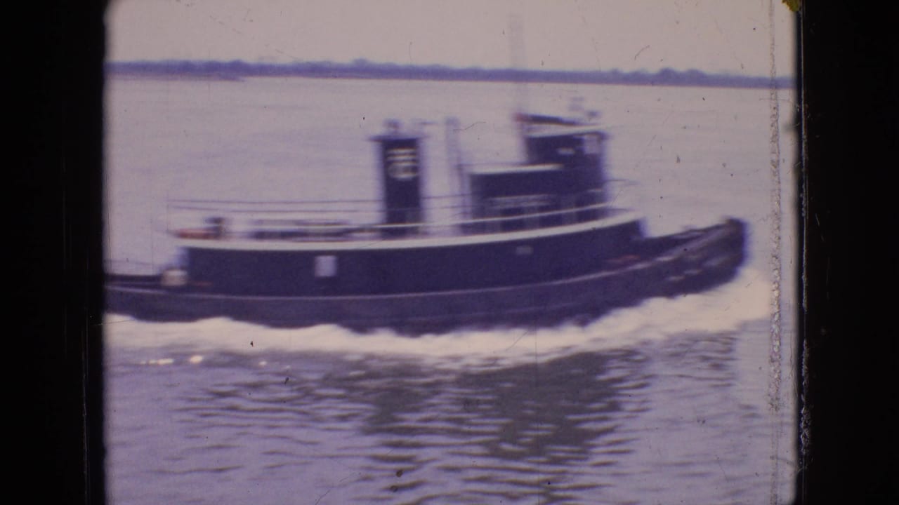 Side view of a tugboat moving on water with wake trailing along its hull.