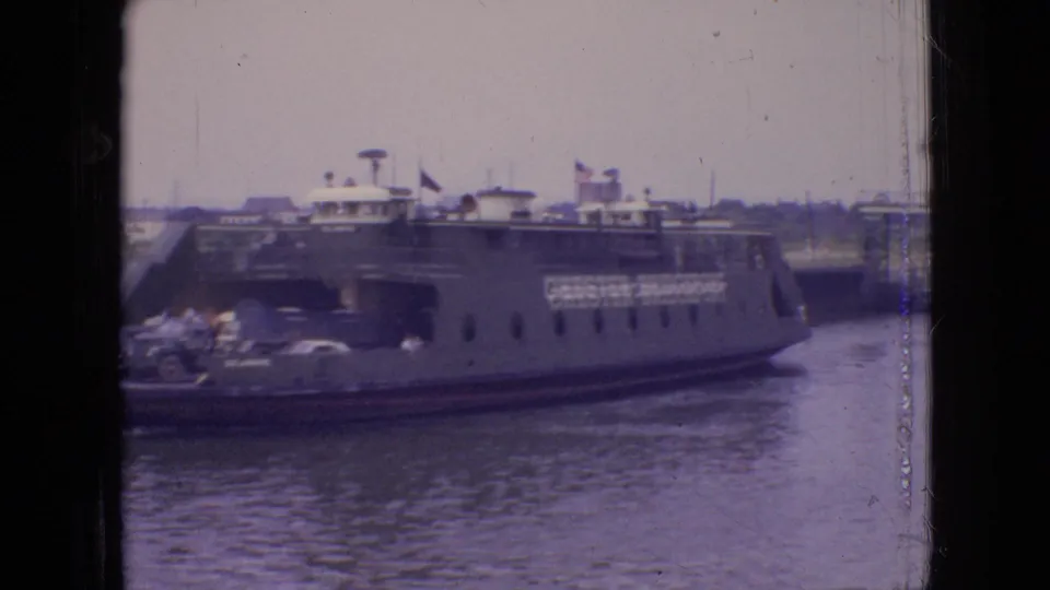 1964 Philadelphia-area frame showing the side of the Chester-Christopher ferry passing through harbor water with automobiles, passengers, flags, and upper deck details visible.
