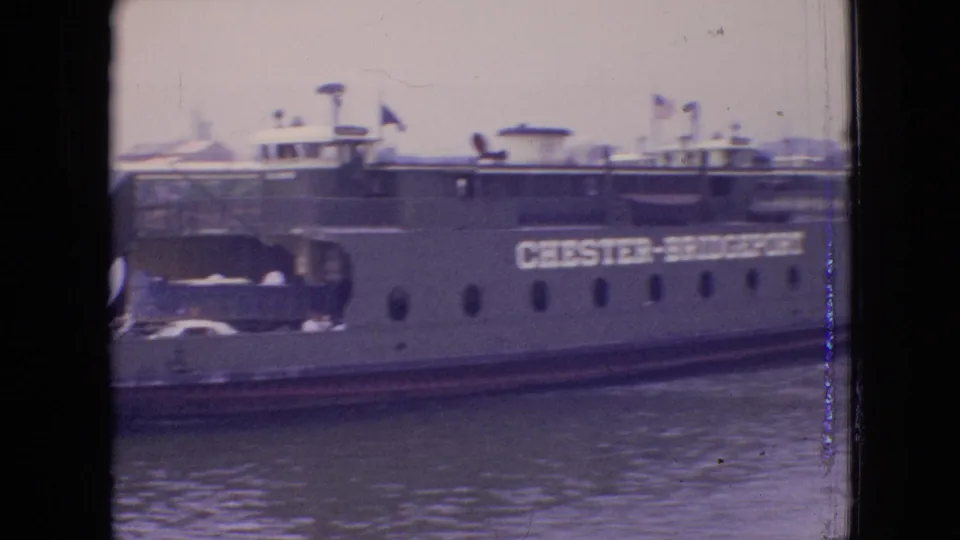 1964 Philadelphia-area frame with the Chester-Christopher name visible on the ferry side, along with portholes, flags, cars partly visible on deck, and rippled harbor water.