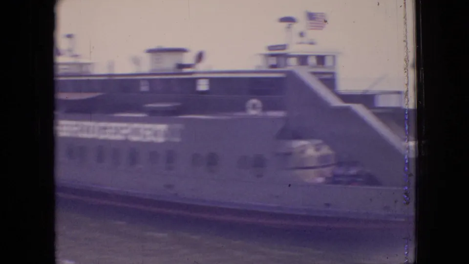 Soft 8mm frame from the 1964 Philadelphia ferry scene showing a close side view of the vessel, partial CHESTER-BRIDGEPORT lettering, deck railings, and water below.