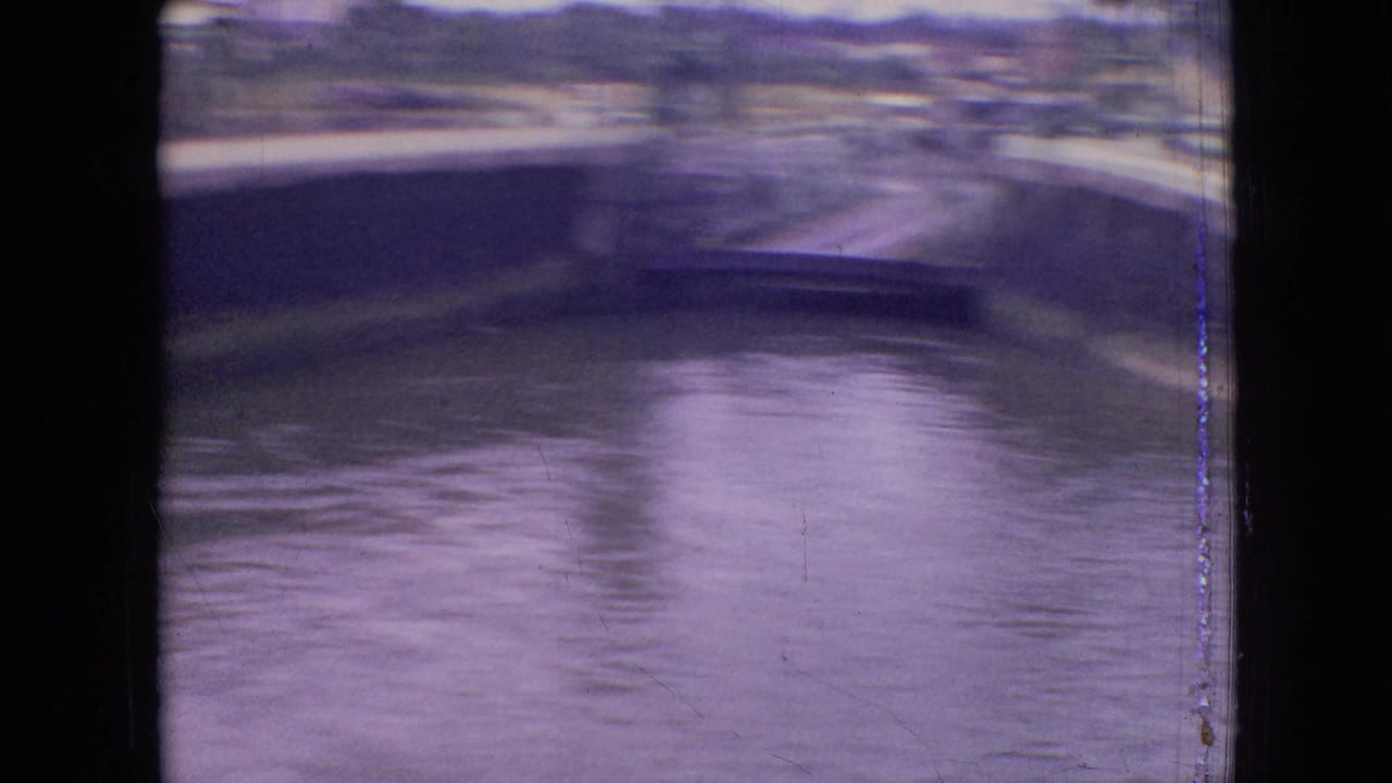 1964 Philadelphia home-movie frame showing canal water, a raised bridge span, retaining walls, and distant buildings in soft 8mm color.