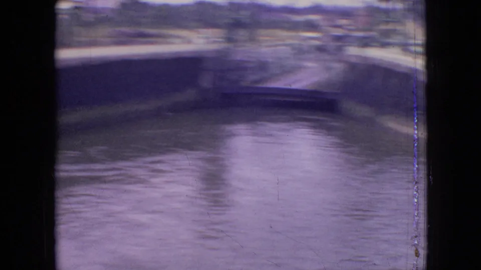 1964 Philadelphia home-movie frame showing canal water, a raised bridge span, retaining walls, and distant buildings in soft 8mm color.