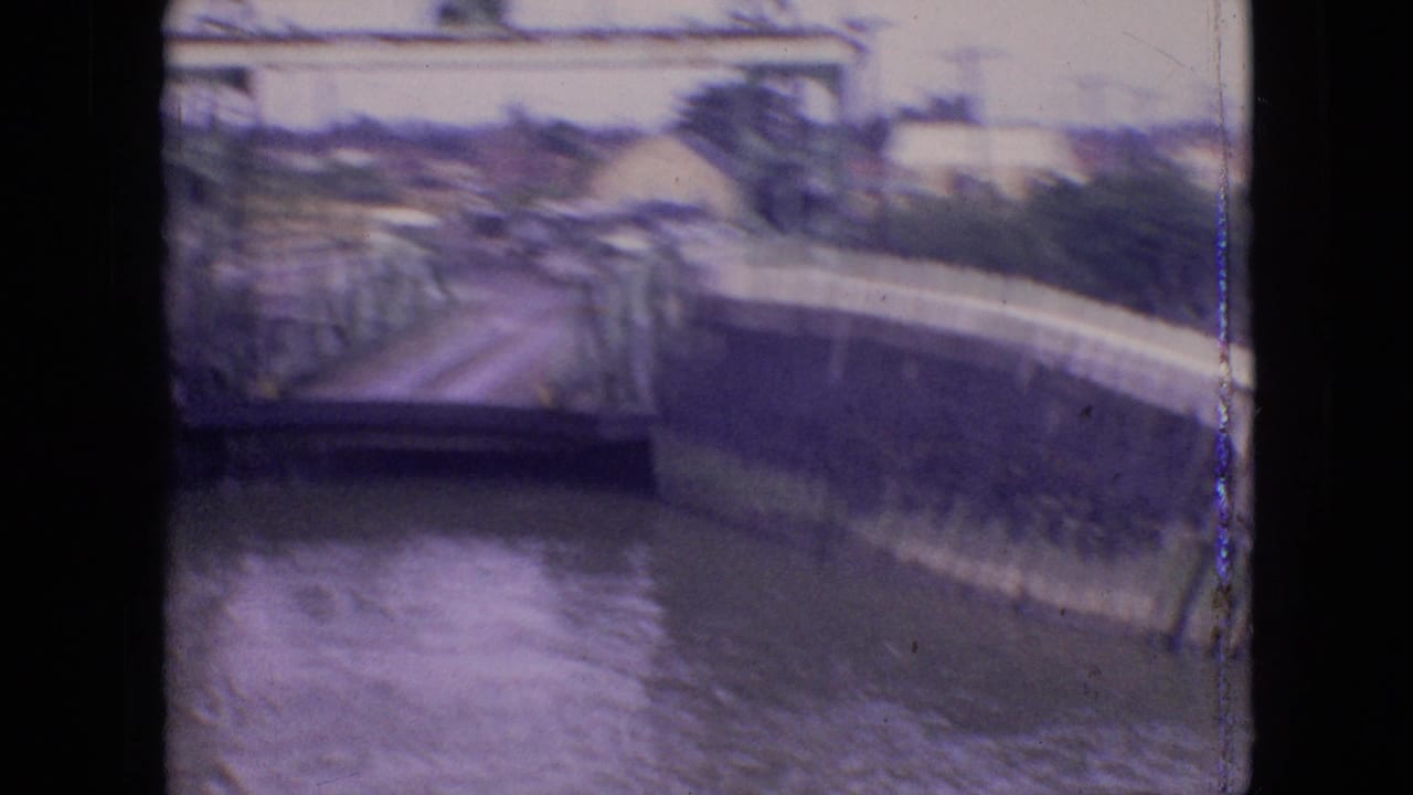 1964 Philadelphia frame with a raised metal bridge over a canal, water below, and urban structures beyond the crossing.