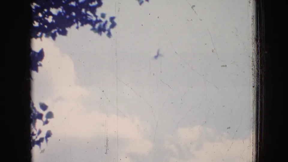 A 1965 New Jersey 8mm frame showing pale clouds and blue sky seen through dark frame edges, with tree leaves visible near the top left.