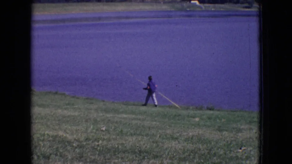 A lakeside fishing scene shows a person carrying a rod along the grassy bank, with the lake filling most of the frame.