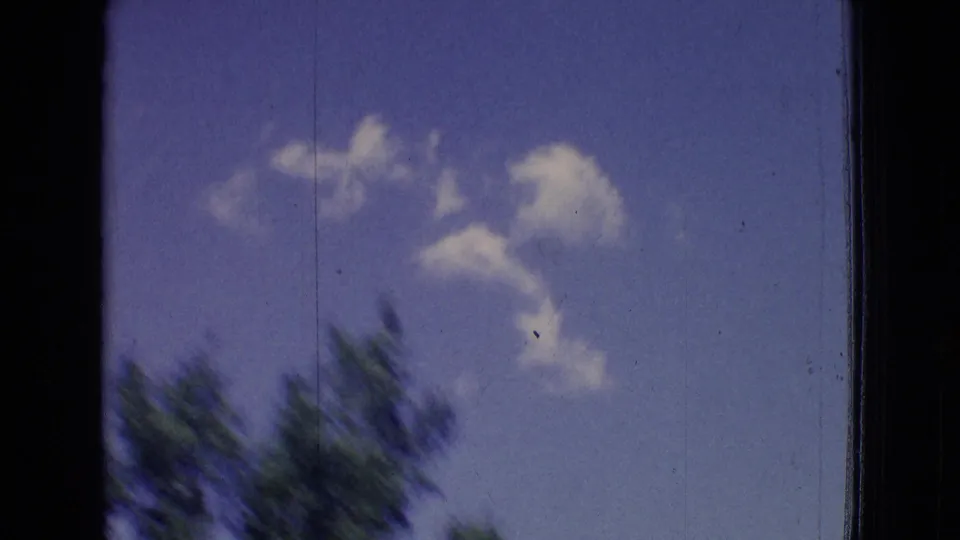 1965 New Jersey 8mm frame with blurred treetops at the lower edge and scattered white clouds in a blue sky during a moving-car shot.