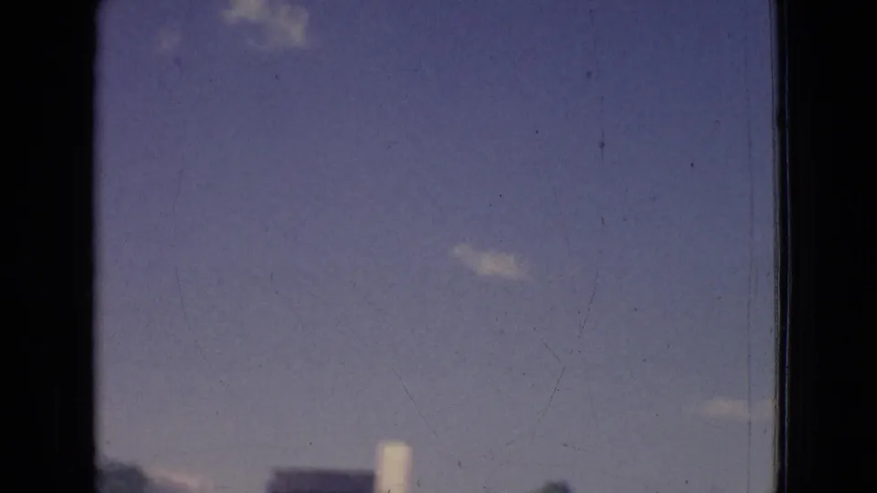 1965 New Jersey 8mm frame with open sky, a few small clouds, and faint distant roadside structures along the lower edge.