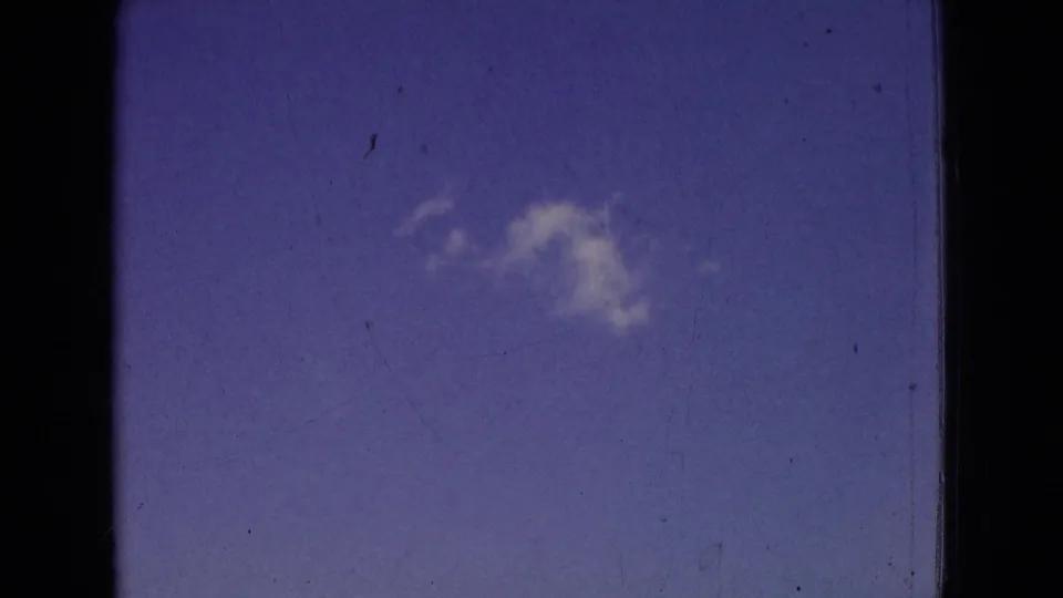 End frame from the 1965 New Jersey 8mm road clip showing mostly blue sky with a small cloud, dark film borders, dust, and vertical scratch marks from the scanned home-movie source.
