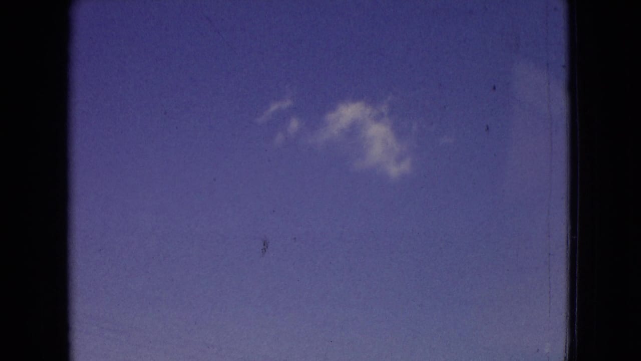 1965 New Jersey 8mm frame showing a clear blue sky and a single soft white cloud, bordered by dark film gate edges and visible surface wear.