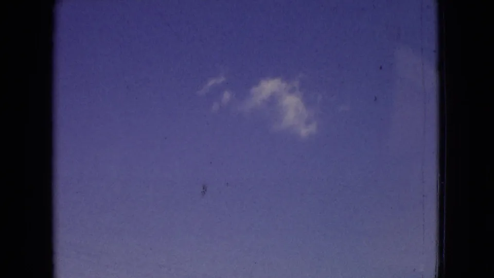 1965 New Jersey 8mm frame showing a clear blue sky and a single soft white cloud, bordered by dark film gate edges and visible surface wear.
