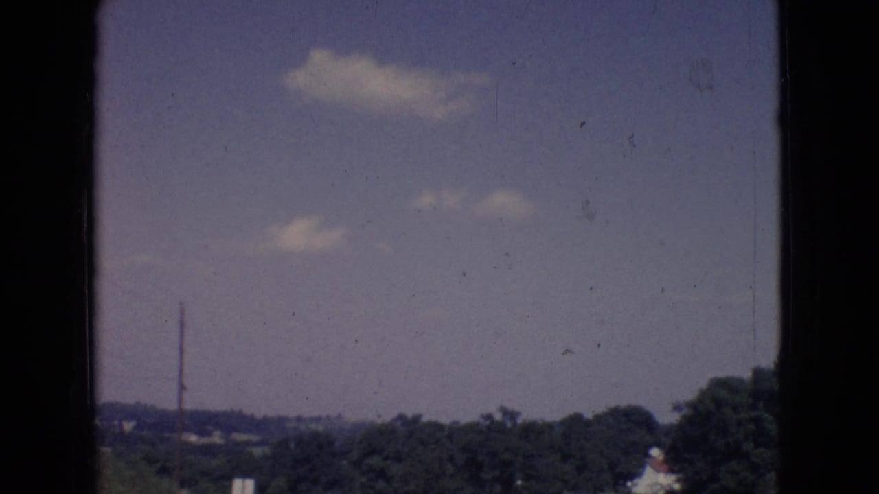 1965 New Jersey home-movie frame showing scattered clouds above a distant rural landscape, with visible 8mm gate edges and film wear.