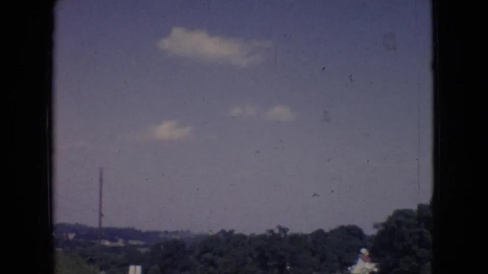 1965 New Jersey home-movie frame showing scattered clouds above a distant rural landscape, with visible 8mm gate edges and film wear.