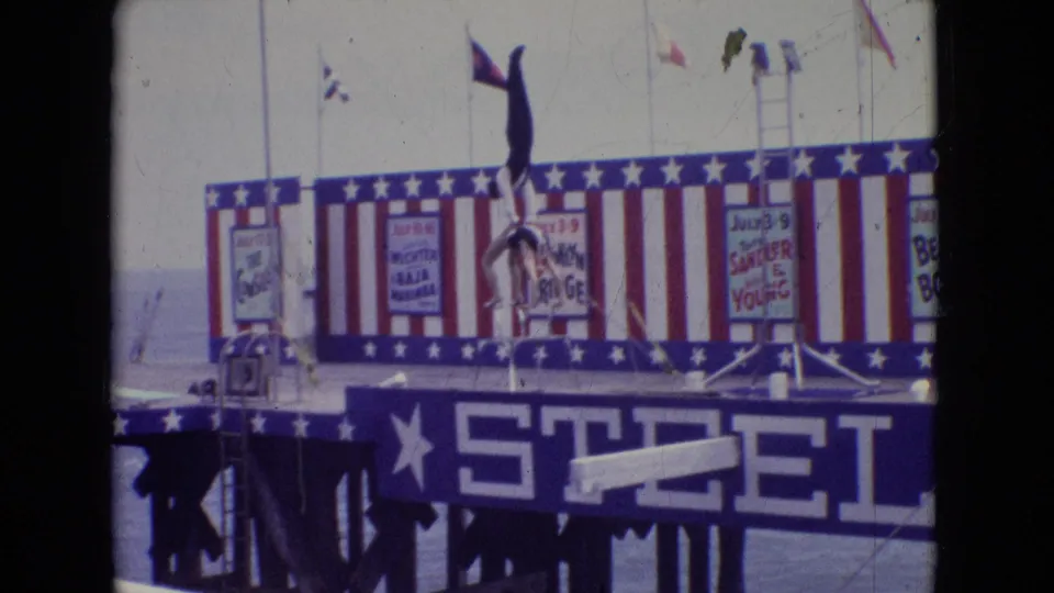 1965 New Jersey 8mm frame showing the female performer in a vertical handstand position supported by the male acrobat on the Steel Pier stage.
