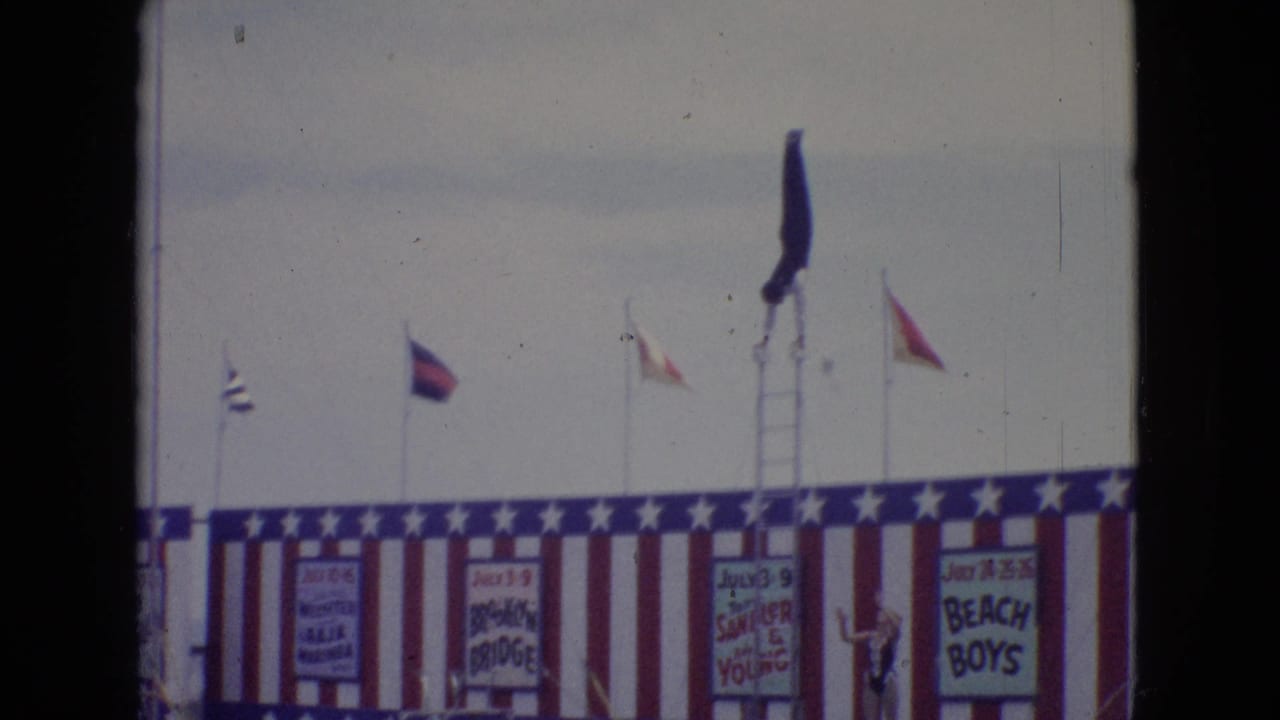 Tall ladder and flags rise above a red, white, and blue seaside stage.