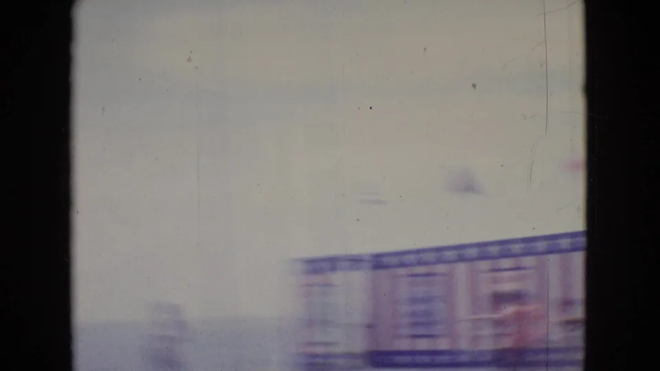 The home-movie camera briefly loses exposure and focus, leaving a washed, blurred glimpse of the seaside stage and water during the pier performance.