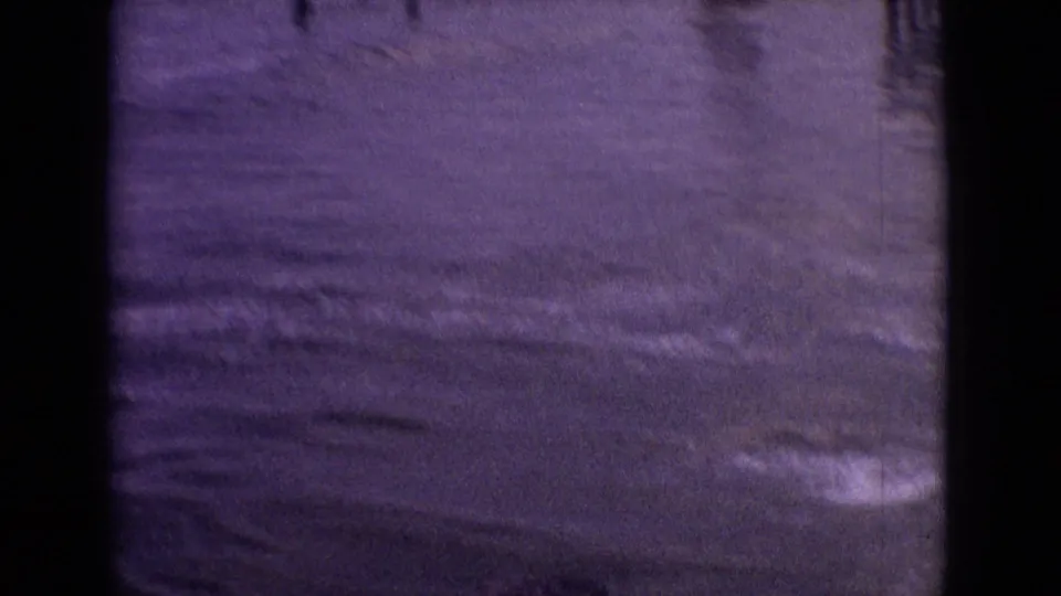 1965 New Jersey 8mm frame showing subdued purple-tinted water and faint shoreline foam, with little identifiable detail beyond the surf texture.