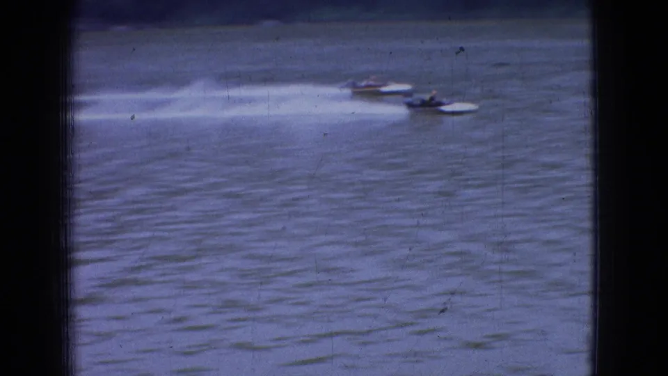 1965 New Jersey 8mm frame showing two small speedboats running side by side across open river water with bright wakes trailing behind them.