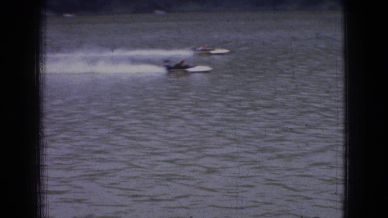 Distant powerboats speed across a wide New Jersey river in 1965 home-movie footage, leaving pale wakes on the water.