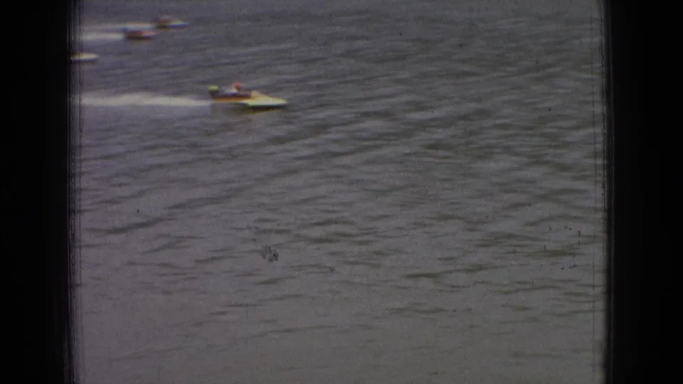 A small open motorboat speeds over the river in the foreground while other boats appear in the distance in this 1965 New Jersey 8mm frame.
