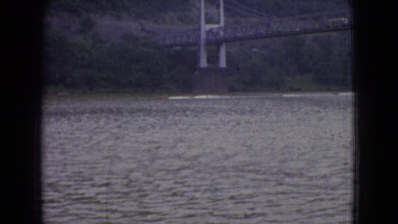 1965 New Jersey 8mm frame showing a distant suspension bridge over a wide body of rippled water, partially obscured by dark window-like borders.