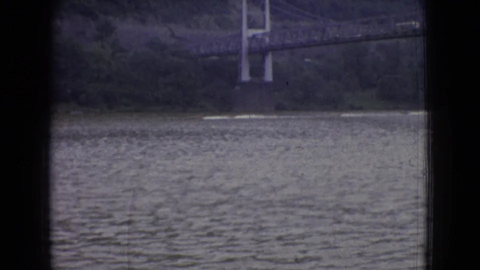 1965 New Jersey 8mm frame showing a distant suspension bridge over a wide body of rippled water, partially obscured by dark window-like borders.