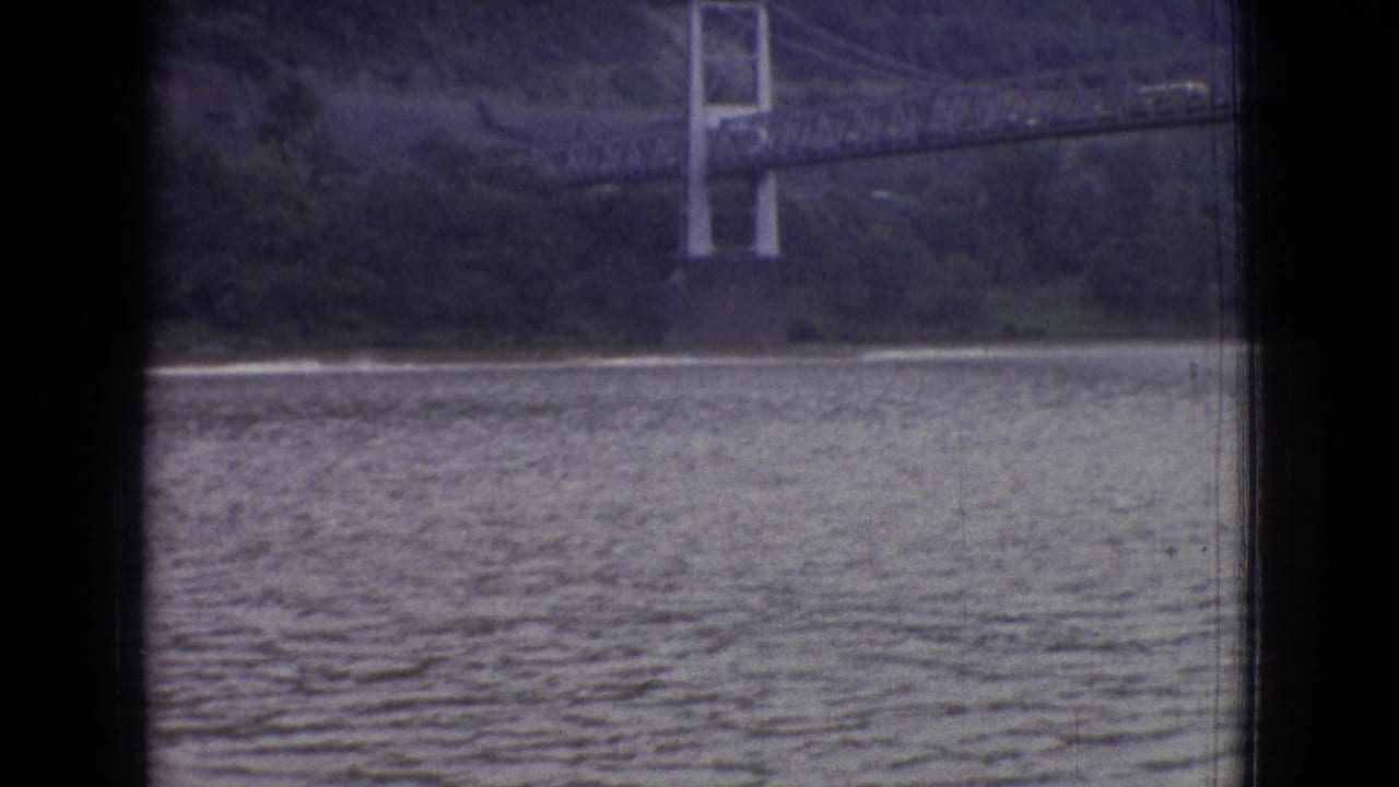 Suspension bridge and shoreline across rippled water, framed by dark borders.