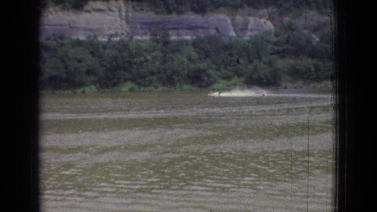 Distant speedboat moving across the river below a wooded bank.