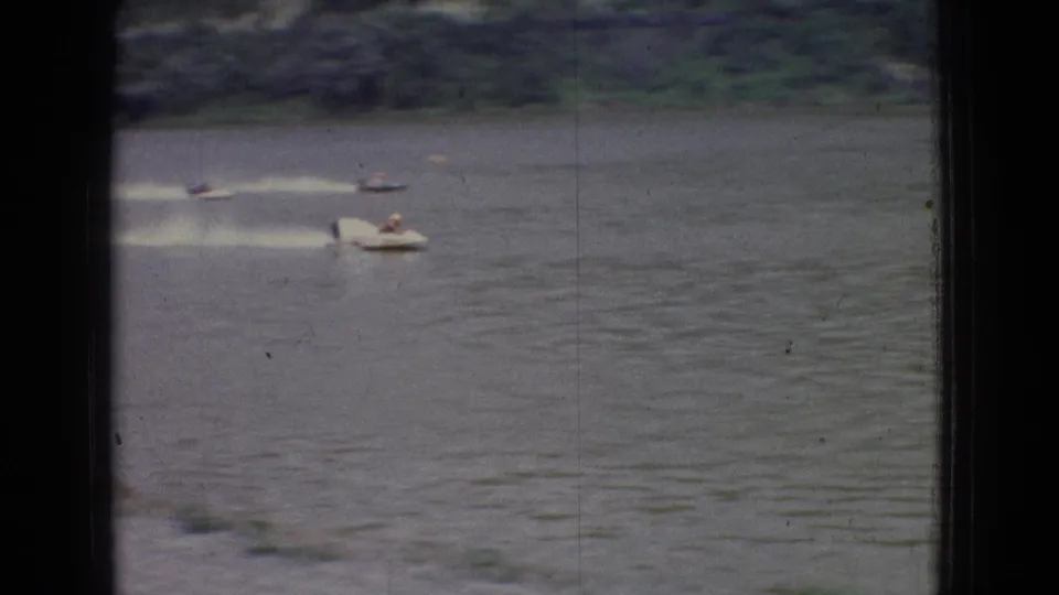 1965 New Jersey river race frame showing multiple small motorboats with tiny riders, spread across the water and trailing bright wakes.