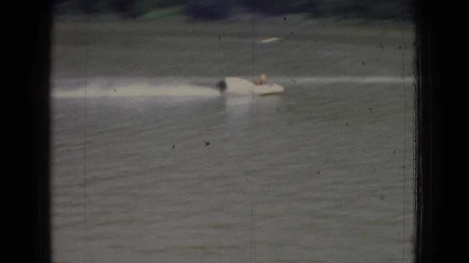 A white speedboat with a distant rider speeds across rippled New Jersey lake water, leaving a bright wake in color 8mm footage from 1965.