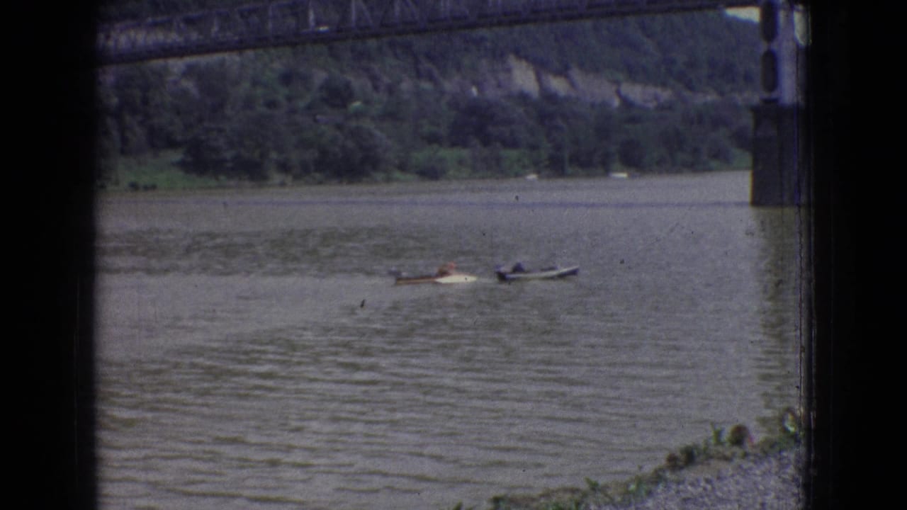Two small boats on a river near a steel bridge pier and wooded bank.