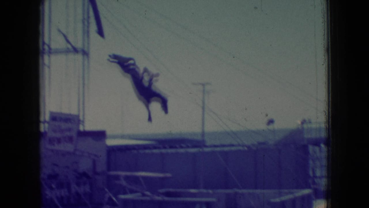 1965 New Jersey 8mm frame showing a dark horse midair after launching near a wooden seaside platform, with water, utility poles, and film gate edges visible.