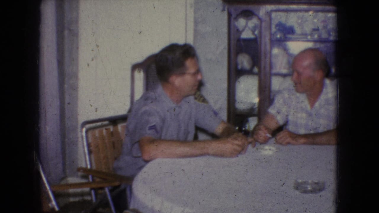 Two men seated at a table beside a china cabinet.