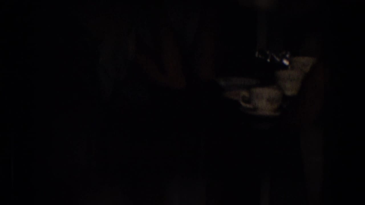 Dark 1965 New Jersey home-movie frame showing a dim domestic table area with a cup and saucer partly visible, though most figures are obscured by shadow.