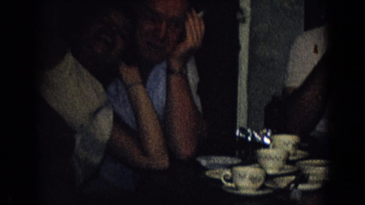 Adults sit close together at a table with teacups and saucers.