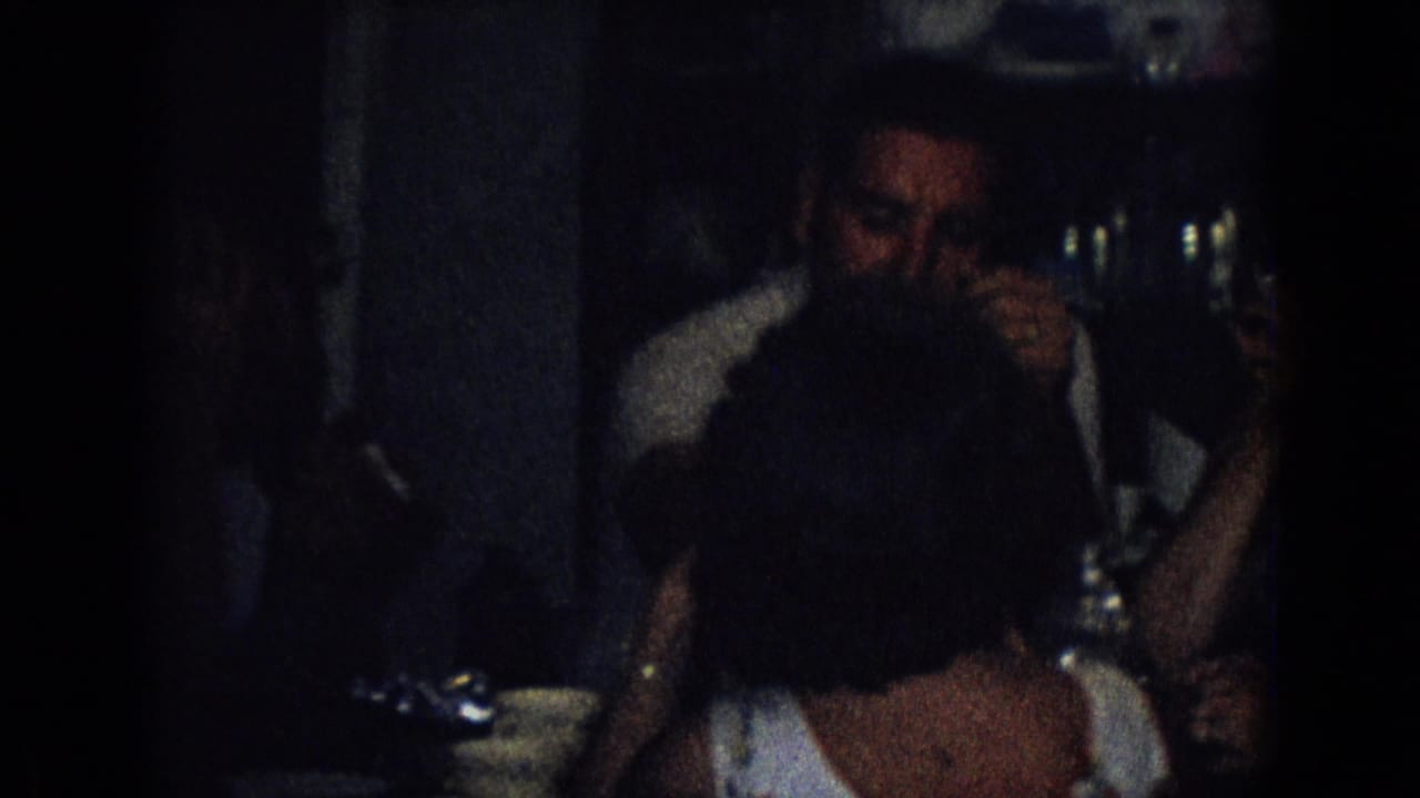 Man and woman sit across a table in a dark indoor room.