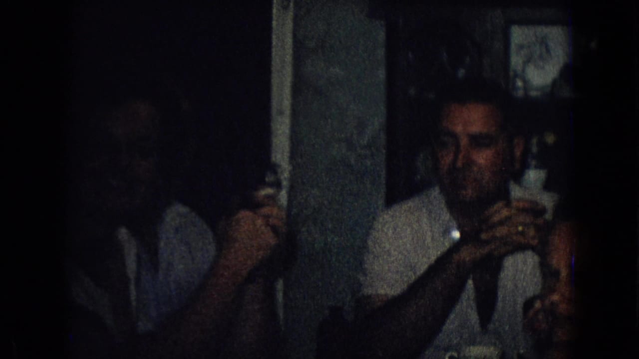 Man in a light shirt sits beside a dark vertical partition while holding a glass.