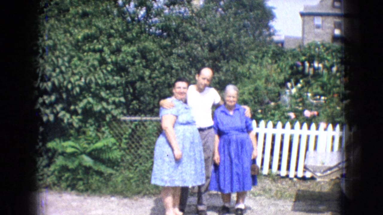 Three adults pose together in a backyard near a white picket fence.