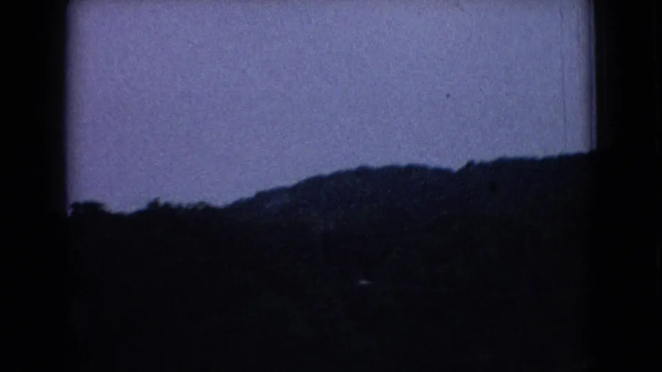 A dim, soft 8mm view of a wooded ridge or treeline during the 1965 New Jersey road-trip sequence.