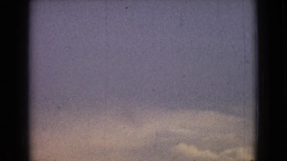 A soft, blurred frame shows the roadway and yellow center markings from inside or near a moving vehicle during the 1965 road-trip footage.